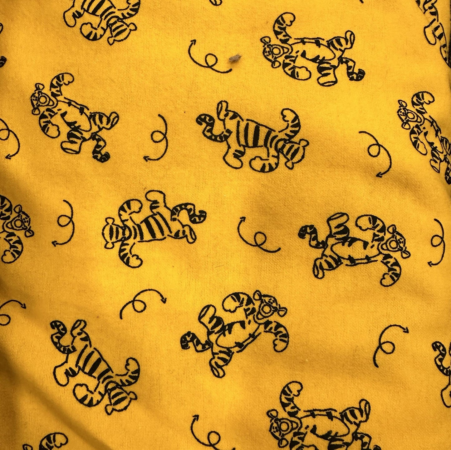 Yellow cotton flannel fabric with repeating Tigger characters and black swirl accents