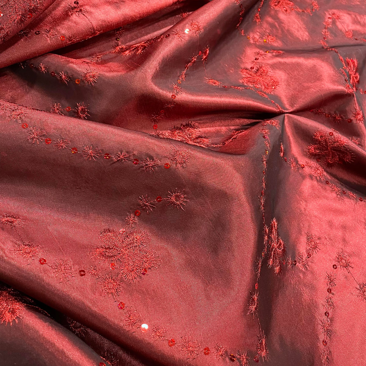 Red polyester taffeta fabric with floral sequin embellishment and a crisp lustrous surface