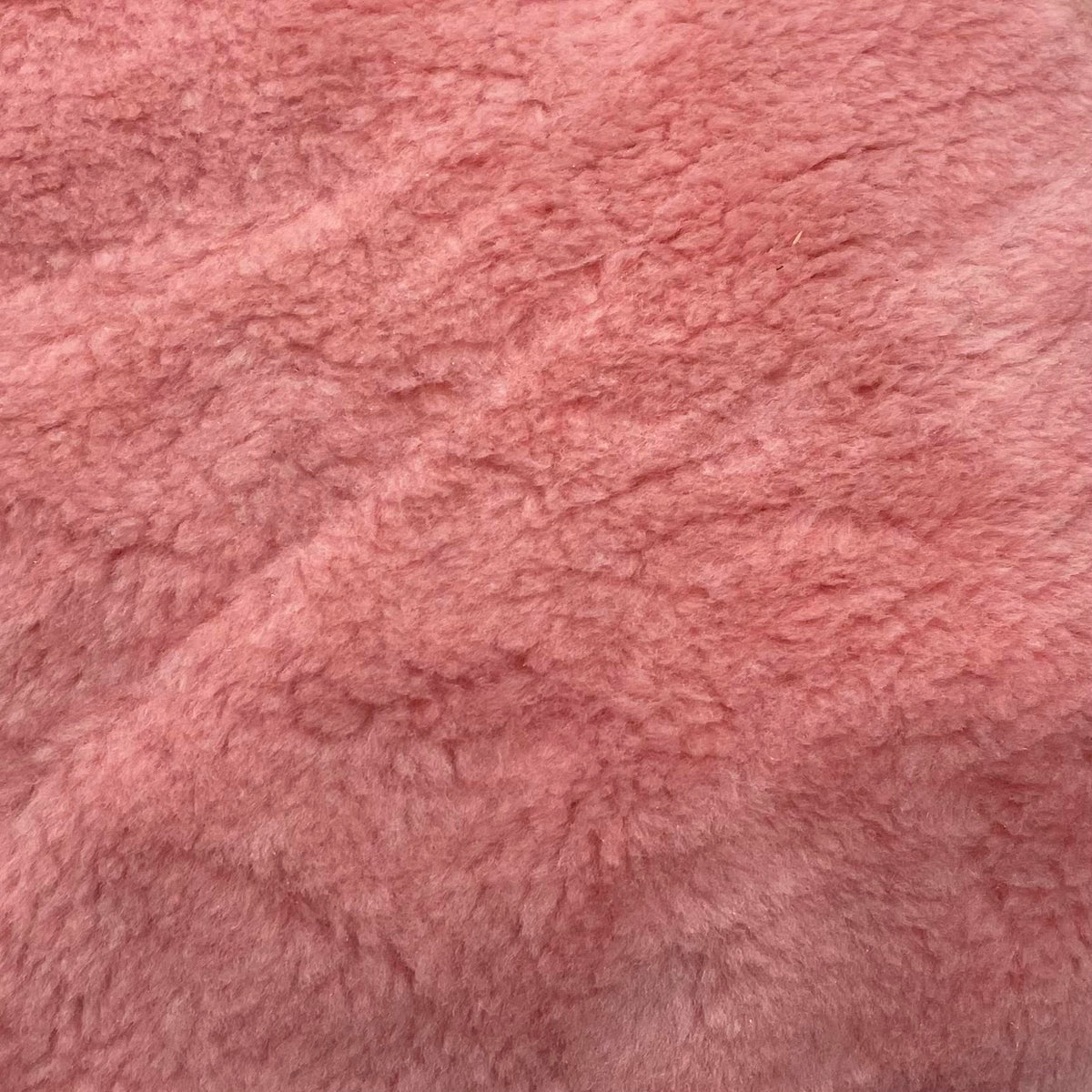 Pink plush polyester sherpa fabric with a soft fluffy texture